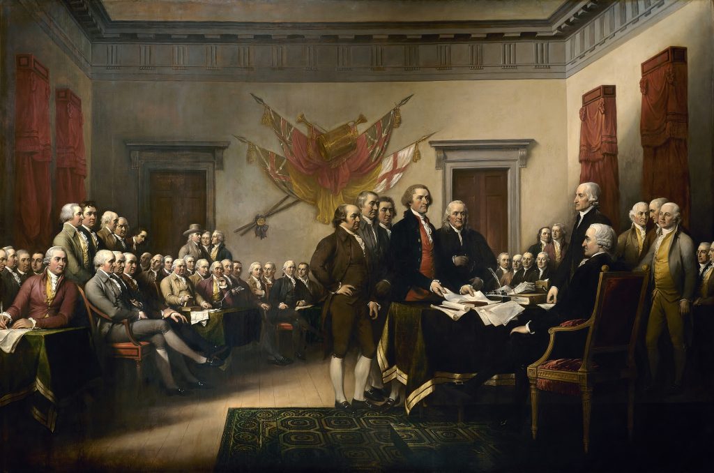| 1776 | 1791 patriot shops group of 18th‑century men in formal attire gathered around a long table in a grand room, some seated and signing documents, with red drapes and banners on the walls.